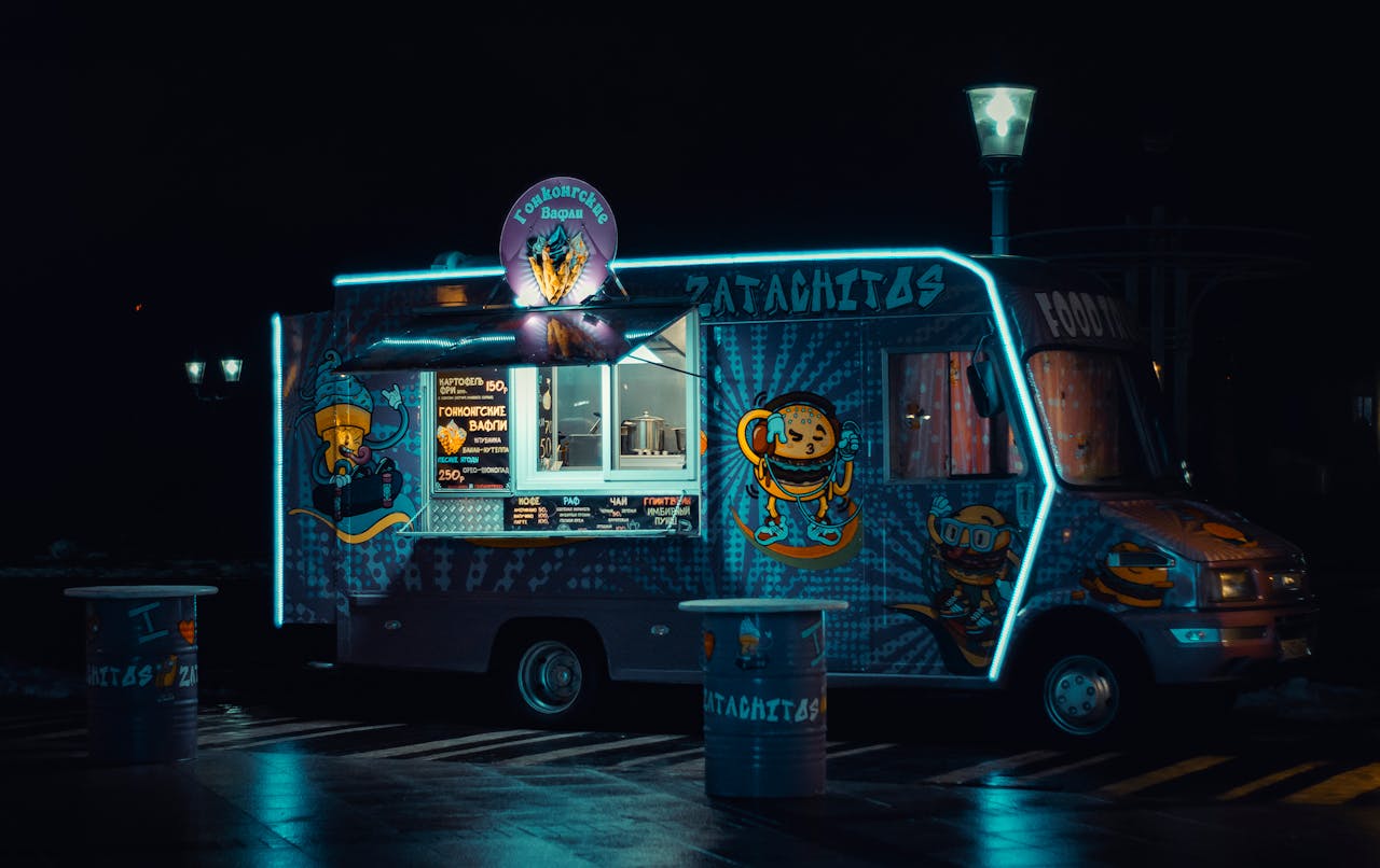 Colorful food truck glowing with neon lights during nighttime.