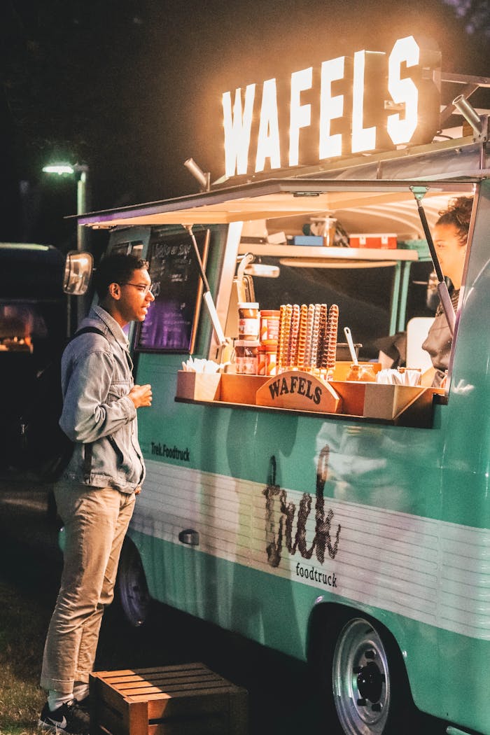 A customer waits at a vibrant waffle food truck in Weert, Netherlands at night.